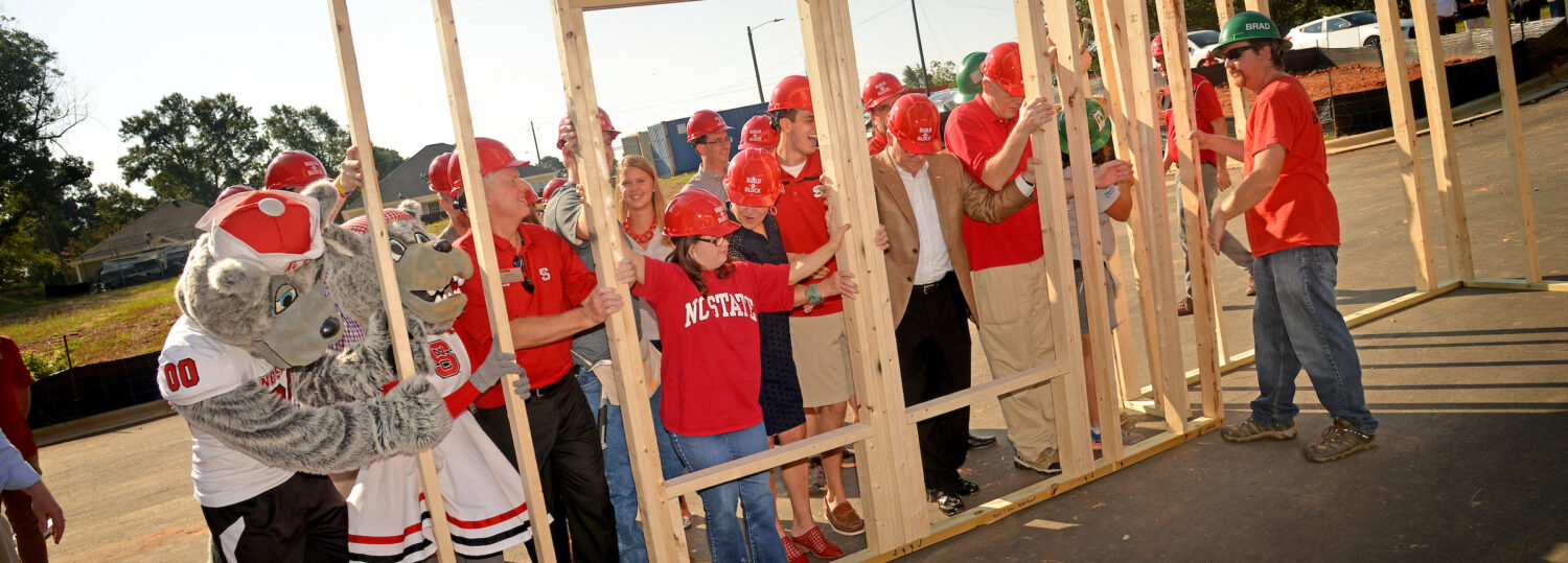 Chancellor Randy Woodson and other NC State participants and volunteers raise wall during the Build-A-Block Habitat for Humanity project ceremony.