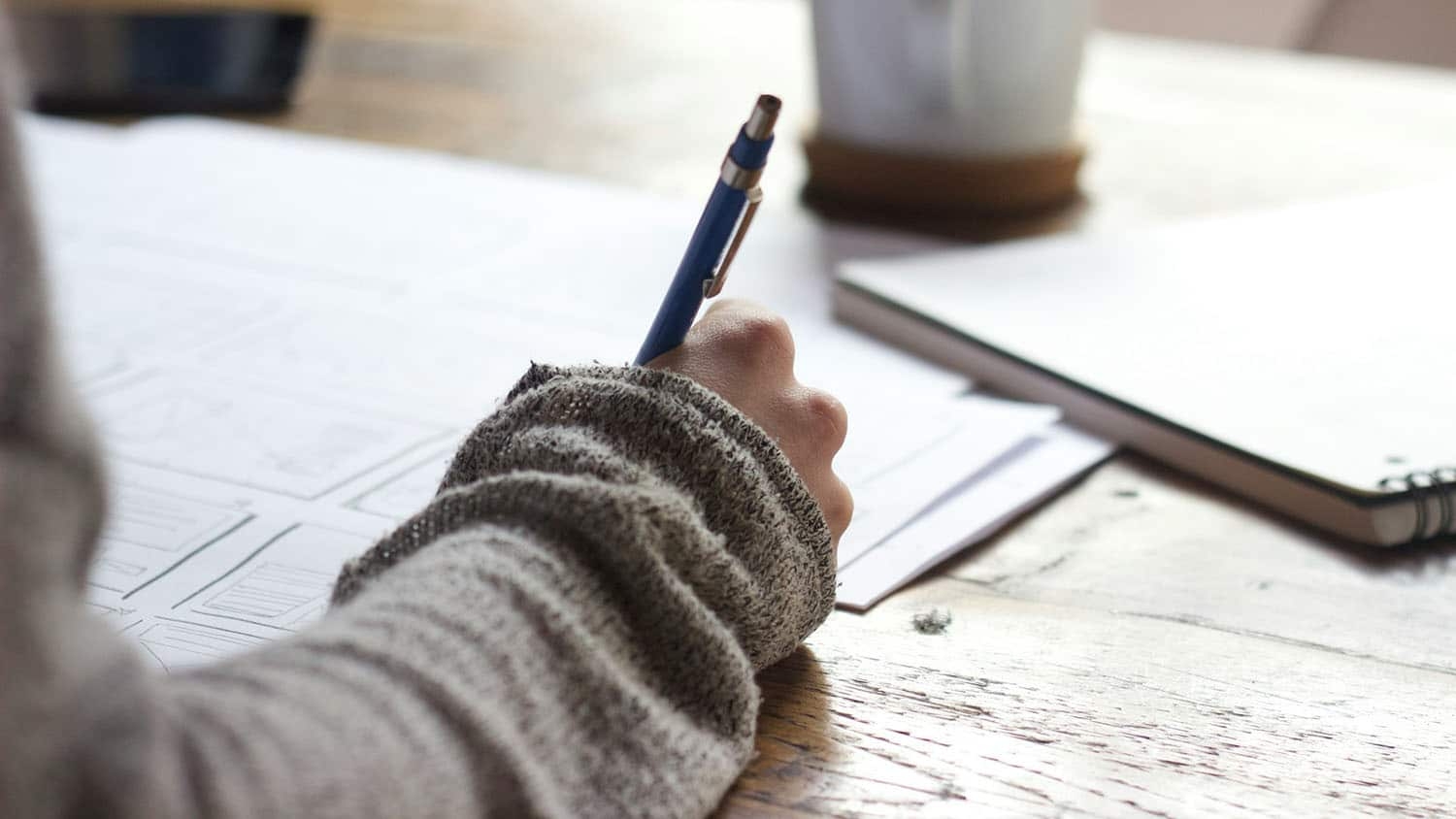 a person wearing a sweater takes notes at a wooden desk