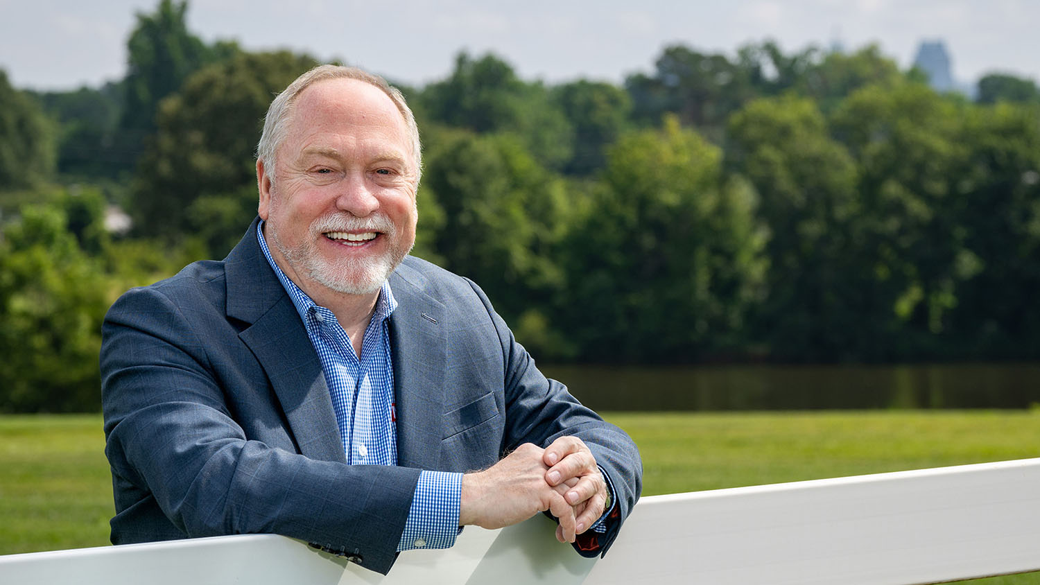 Vice Provost David Monks leaning against a white fence in a grassy field