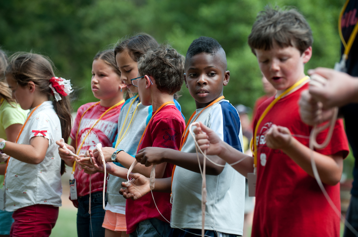 A group of kids hold a stretched-out piece of silly putty during a STEM camp